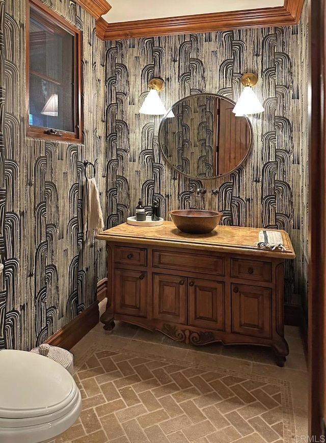 half bath featuring brick floor, vanity, toilet, and wallpapered walls