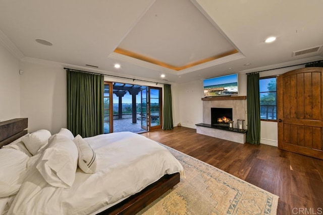 bedroom featuring wood finished floors, crown molding, a premium fireplace, a raised ceiling, and access to exterior