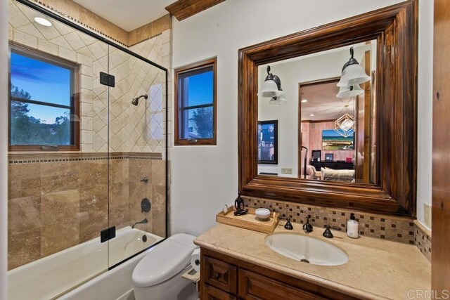 bathroom with backsplash, bath / shower combo with glass door, vanity, and toilet