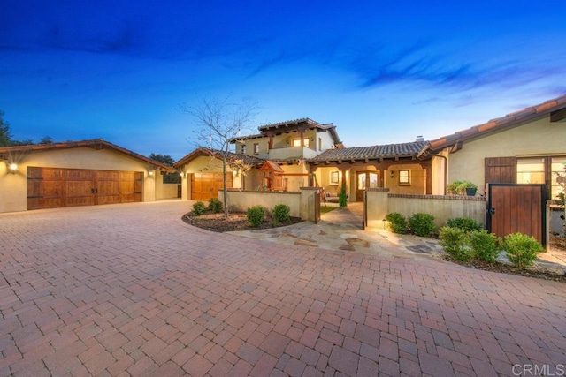 mediterranean / spanish-style house featuring a fenced front yard, a tile roof, stucco siding, decorative driveway, and an attached garage