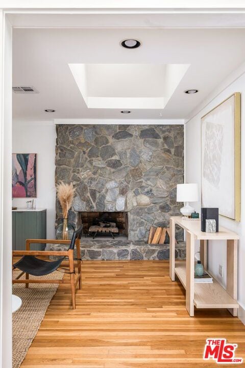 interior space with hardwood / wood-style floors, a stone fireplace, and a raised ceiling