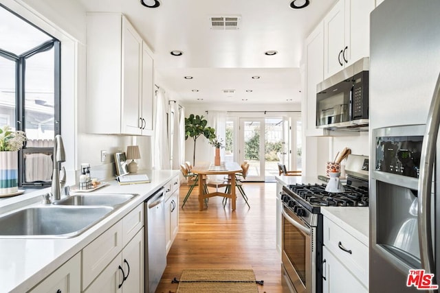 kitchen featuring french doors, sink, white cabinetry, light wood-type flooring, and appliances with stainless steel finishes