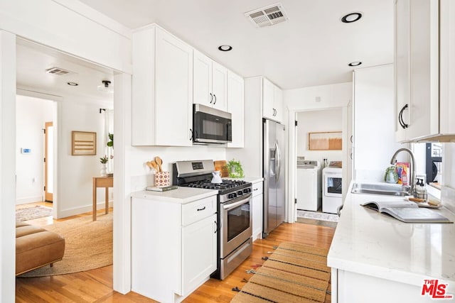 kitchen with stainless steel appliances, washing machine and clothes dryer, white cabinets, and light wood-type flooring