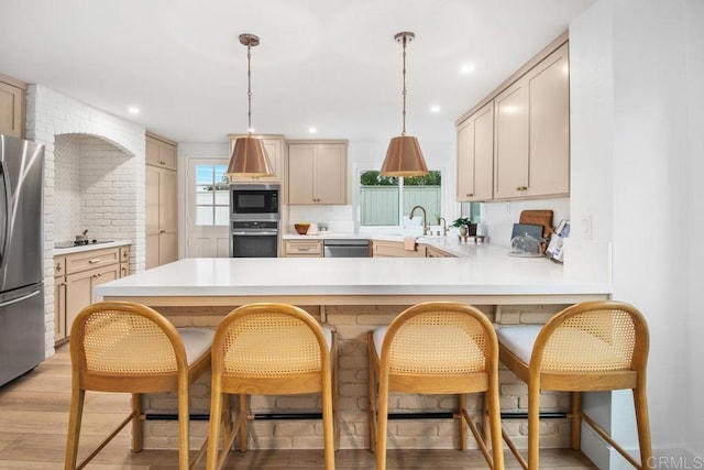 kitchen featuring light countertops, light wood-style flooring, appliances with stainless steel finishes, a peninsula, and a kitchen breakfast bar