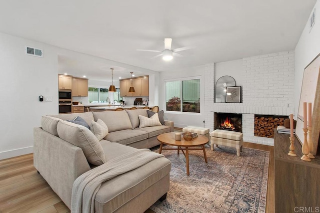 living area featuring baseboards, visible vents, a fireplace, and light wood finished floors