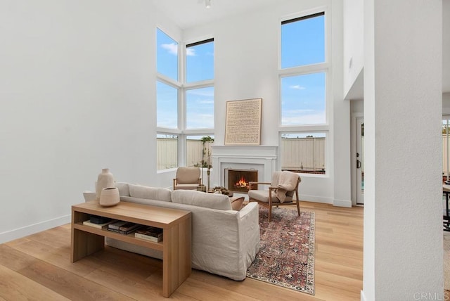 living area with a lit fireplace, a towering ceiling, baseboards, and wood finished floors