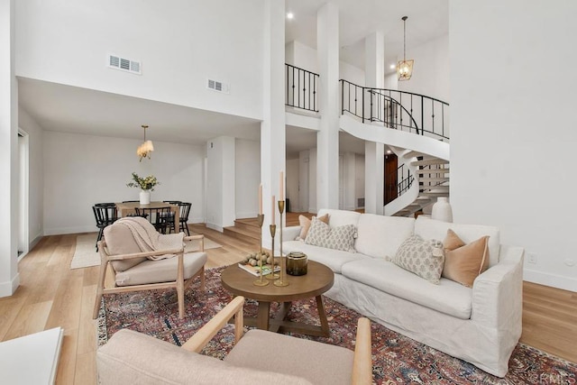 living area with stairs, light wood-type flooring, visible vents, and an inviting chandelier