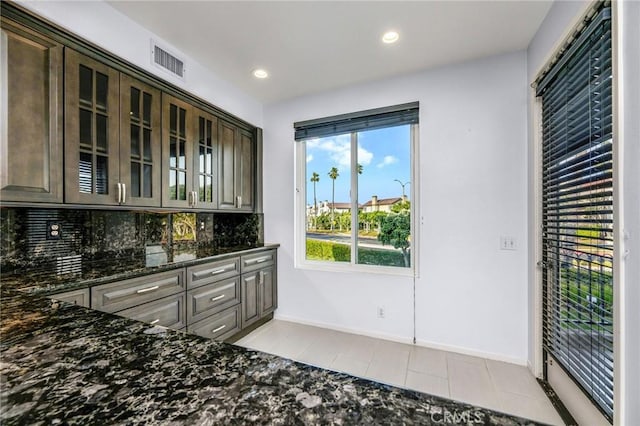 interior space featuring backsplash, light tile patterned flooring, dark brown cabinets, and dark stone countertops