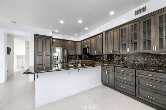 kitchen featuring dark stone countertops, decorative backsplash, stainless steel appliances, and dark brown cabinetry