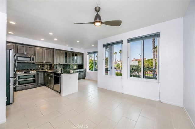 kitchen with sink, ceiling fan, dark stone countertops, stainless steel appliances, and tasteful backsplash