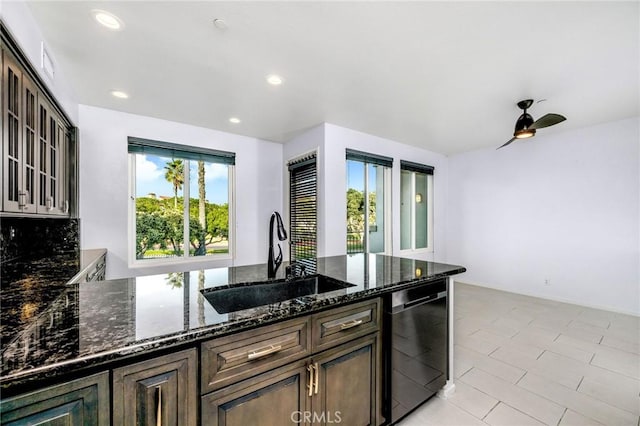 kitchen featuring sink, dark brown cabinets, dark stone countertops, dishwasher, and ceiling fan