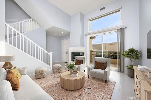 sitting room with a high ceiling, stairway, a fireplace, and visible vents