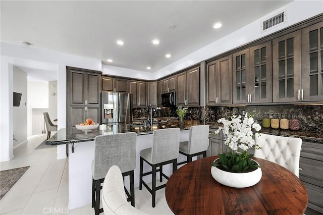 kitchen with dark brown cabinets, black microwave, visible vents, and stainless steel refrigerator with ice dispenser