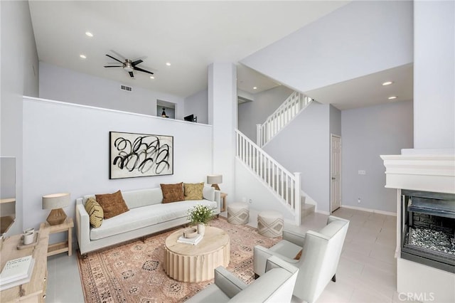 living room featuring stairway, a ceiling fan, a high ceiling, a fireplace, and recessed lighting