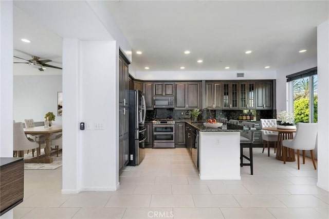 kitchen featuring dark stone countertops, a breakfast bar area, stainless steel appliances, dark brown cabinetry, and tasteful backsplash