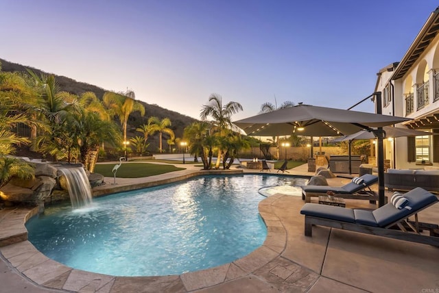 pool at dusk featuring a hot tub, pool water feature, an outdoor living space, and a patio area