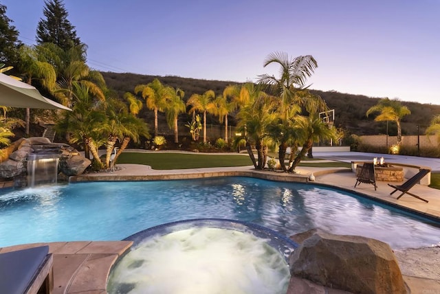 pool at dusk featuring an in ground hot tub, a patio area, and an outdoor fire pit