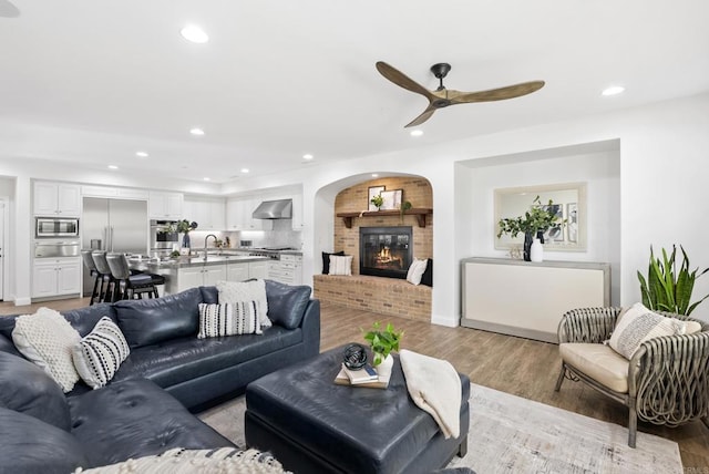 living room with sink, light hardwood / wood-style flooring, a fireplace, and ceiling fan