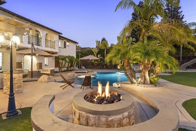 pool at dusk featuring an outdoor fire pit and a patio