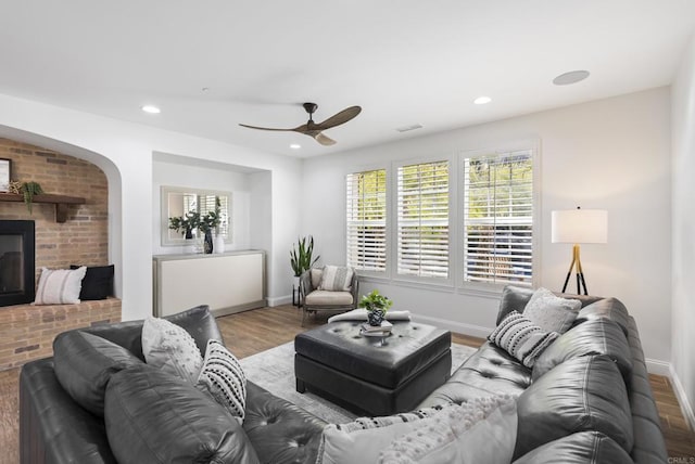 living room featuring a brick fireplace, hardwood / wood-style floors, and ceiling fan