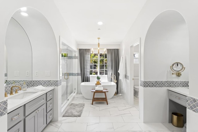 full bathroom with tile walls, an inviting chandelier, vanity, shower with separate bathtub, and toilet