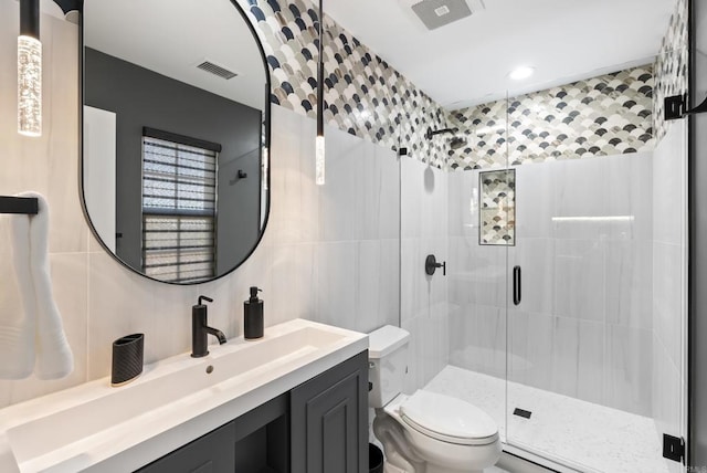 bathroom featuring a shower with door, tile walls, vanity, tasteful backsplash, and toilet