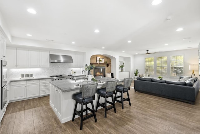 kitchen featuring appliances with stainless steel finishes, white cabinetry, an island with sink, a breakfast bar area, and wall chimney exhaust hood