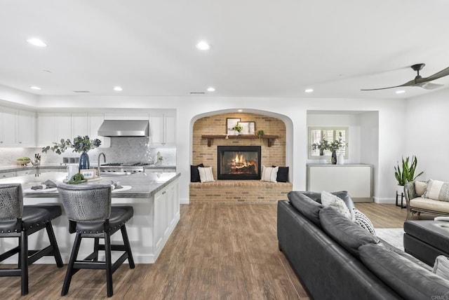 kitchen featuring wall chimney range hood, hardwood / wood-style flooring, white cabinetry, a kitchen breakfast bar, and decorative backsplash