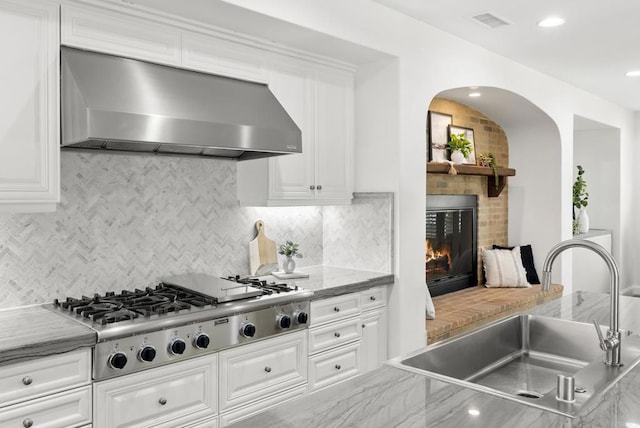 kitchen with wall chimney range hood, sink, tasteful backsplash, stainless steel gas cooktop, and white cabinets