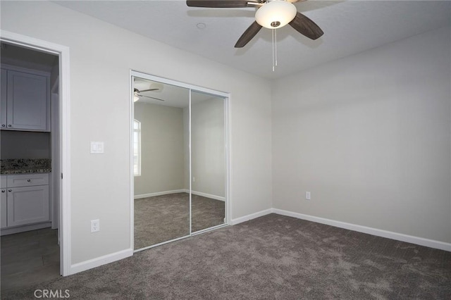 unfurnished bedroom featuring ceiling fan, a closet, and dark colored carpet