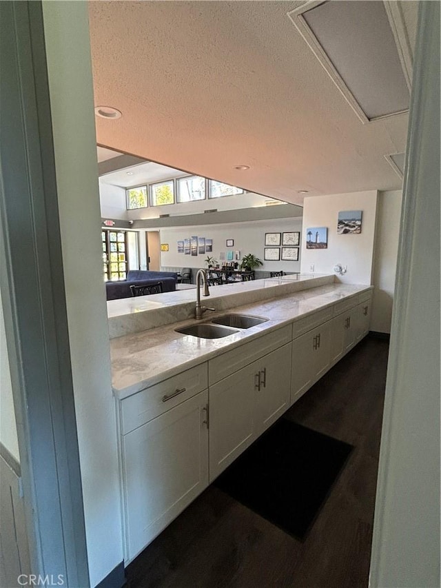 kitchen featuring a textured ceiling, a sink, light stone countertops, and white cabinets