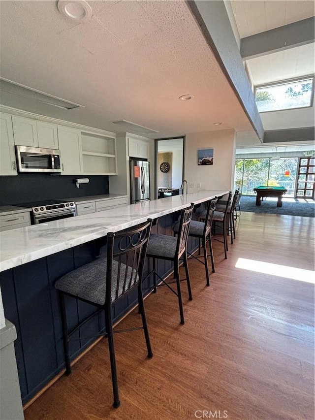 kitchen featuring a breakfast bar, appliances with stainless steel finishes, light stone countertops, hardwood / wood-style floors, and white cabinets