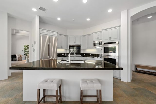 kitchen with a center island with sink, sink, built in appliances, and a breakfast bar