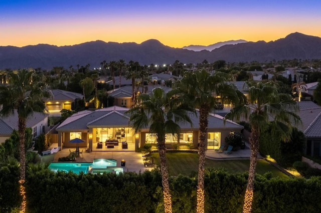 back house at dusk with a mountain view, a patio area, and outdoor lounge area