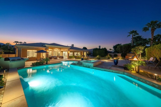 pool at dusk with a patio and an in ground hot tub