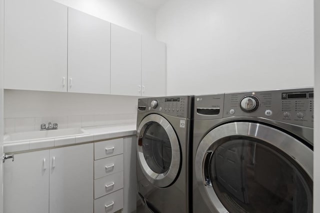 clothes washing area featuring cabinets, sink, and washer and clothes dryer