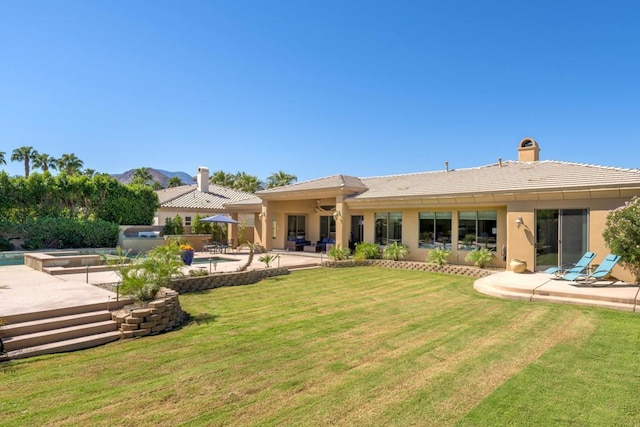 rear view of property with a swimming pool with hot tub, a mountain view, a patio area, and a lawn