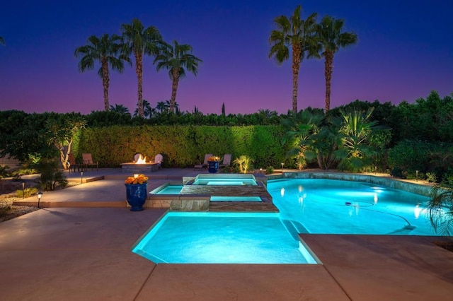 pool at dusk with an in ground hot tub, an outdoor fire pit, and a patio area