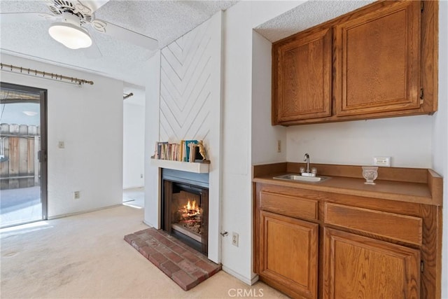 interior space featuring a warm lit fireplace, a textured ceiling, ceiling fan, light carpet, and a sink