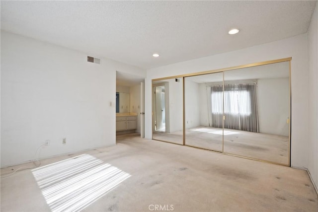 unfurnished bedroom featuring recessed lighting, a closet, visible vents, light carpet, and connected bathroom