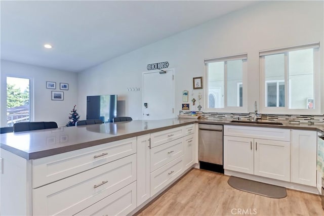 kitchen with sink, light hardwood / wood-style flooring, white cabinetry, stainless steel dishwasher, and kitchen peninsula