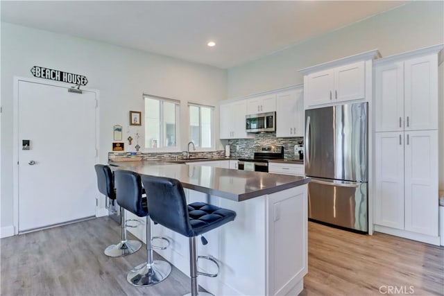 kitchen with sink, white cabinetry, backsplash, stainless steel appliances, and a kitchen breakfast bar