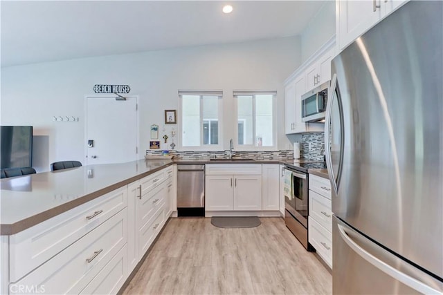 kitchen featuring white cabinetry, sink, light hardwood / wood-style floors, kitchen peninsula, and stainless steel appliances