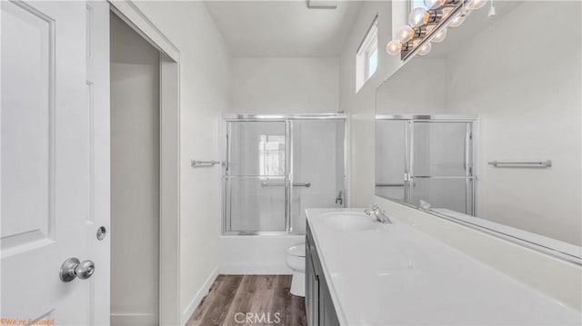 full bathroom with baseboards, toilet, shower / bath combination with glass door, wood finished floors, and vanity