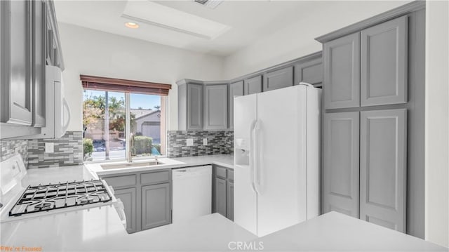 kitchen featuring white appliances, a sink, gray cabinets, light countertops, and backsplash