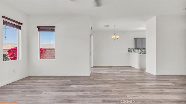 spare room featuring light wood-style floors, a chandelier, visible vents, and baseboards