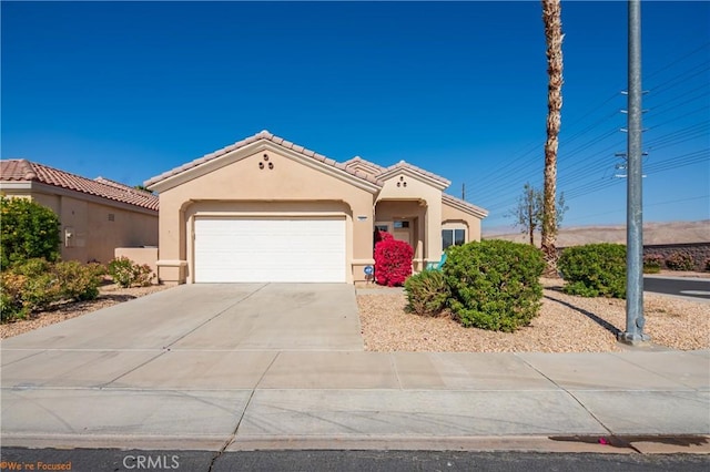 mediterranean / spanish home with an attached garage, a tile roof, concrete driveway, and stucco siding