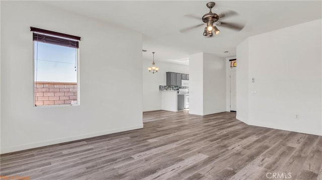 empty room featuring ceiling fan with notable chandelier, wood finished floors, and baseboards