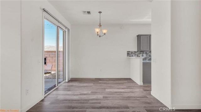 unfurnished dining area with light wood-style floors, visible vents, a notable chandelier, and baseboards