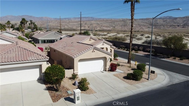 view of front of home with concrete driveway, a tile roof, a mountain view, and stucco siding